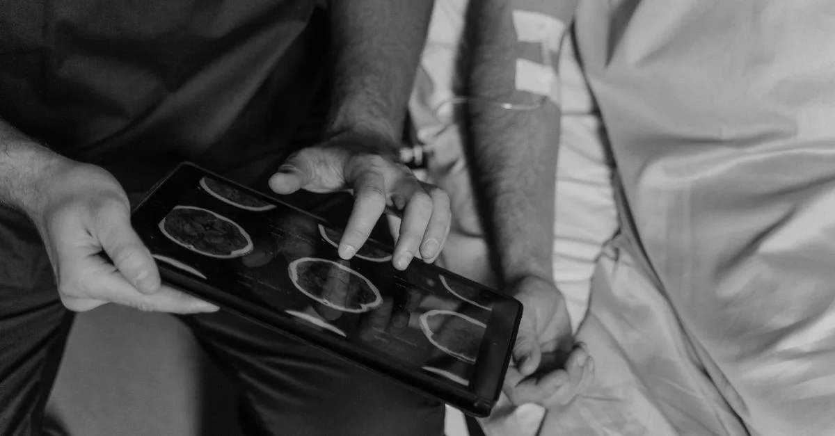 Un professionnel de la santé examine les scanner CT d'un patient sur une tablette numérique en niveaux de gris.