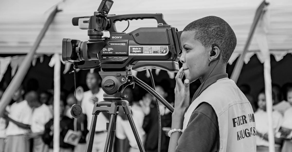 Un jeune utilise une caméra vidéo professionnelle lors d'un événement communautaire en intérieur.