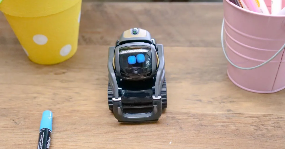 Un petit robot moderne placé sur un bureau en bois entouré de fournitures de bureau, illustrant une technologie innovante.