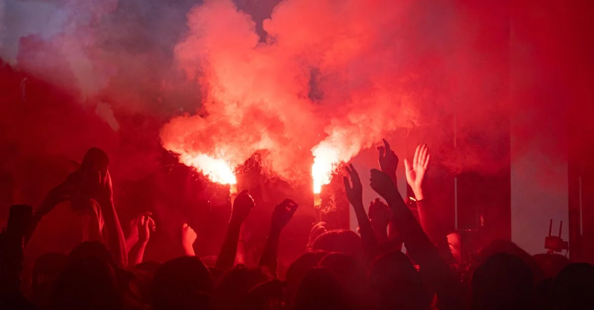 Scène animée d'une foule joyeuse célébrant avec des fumigènes rouges dans la nuit.