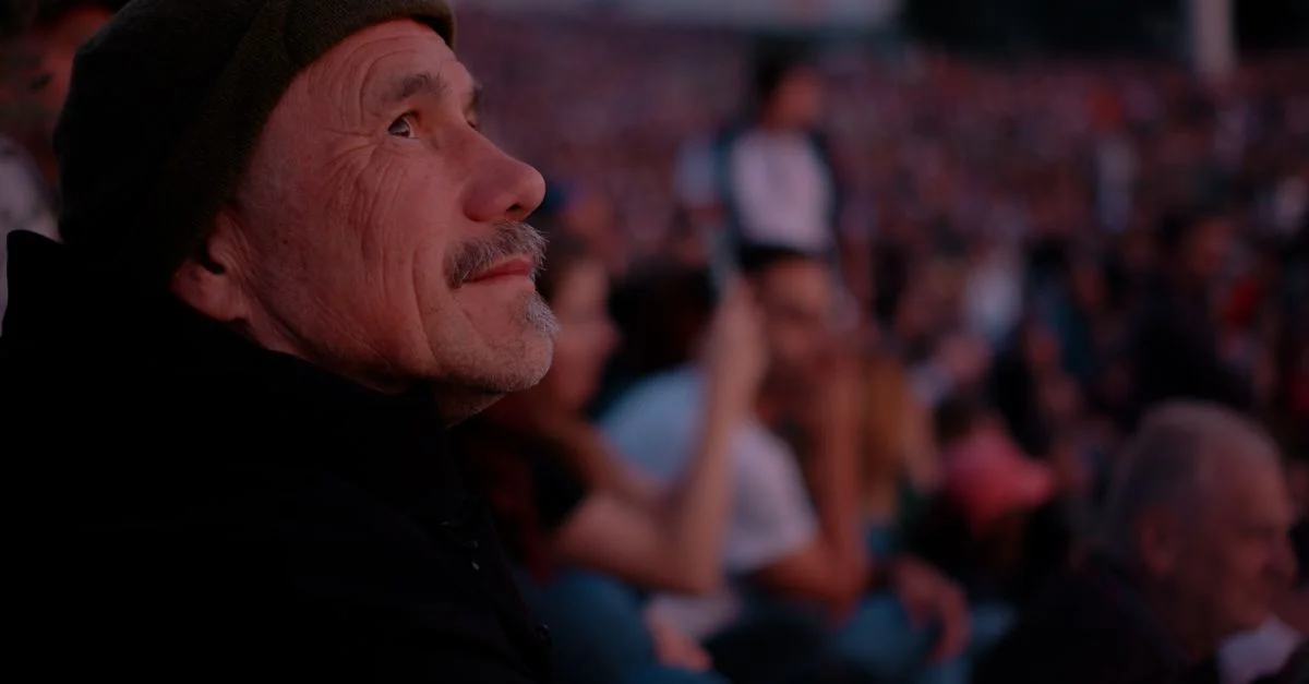 Un homme âgé est assis au milieu d'une foule, captivé par un concert en plein air au crépuscule à Bratislava.